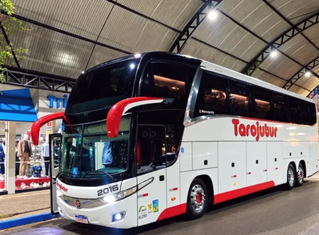 Ônibus da Tarojutur com a porta aberta em um terminal coberto e iluminado, à noite
